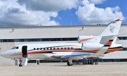 Photo of Falcon 900 with open door sitting in front of a Duncan Aviation hangar painted in white with orange and navy stripe
