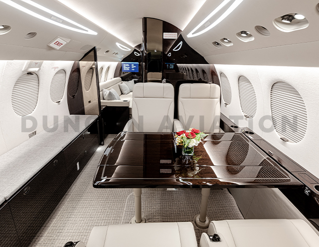 Beautifully refurbished interior of Falcon 7X showing cream leather chairs and dark wood table with cream and dark wood accents throughout